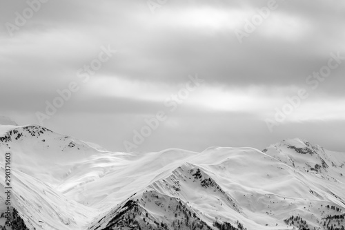 Sunlight snowy mountains in fog and gray overcast sky