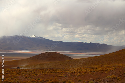Hills with brown soil in the foreground, a lake in the middle and mountains under a stormy sky in the background. Bolivia desert highlands, Potosi region 