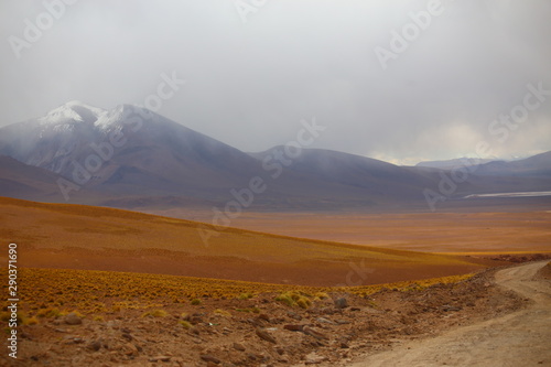 Hills with light brown soil in the foreground and mountains under a stormy sky in the background. Bolivia desert highlands, Potosi region 