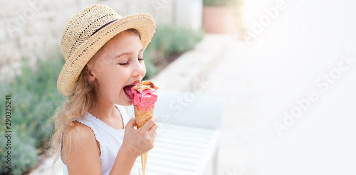 Kid is eating ice cream. Happy Little girl is enjoying italian gelato in town. Cute child in straw hat is tasting delicious street food in summer travel outdoors. Light background, free space for text