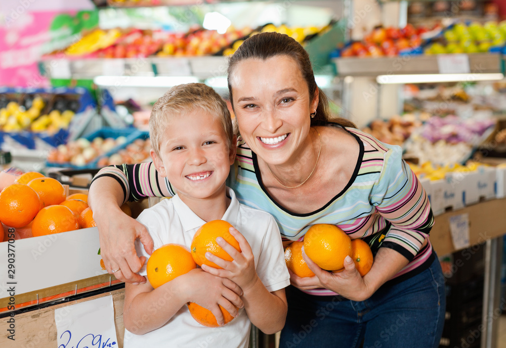 Fototapeta premium Portrait of happy woman and her little son choosing oranges at shop