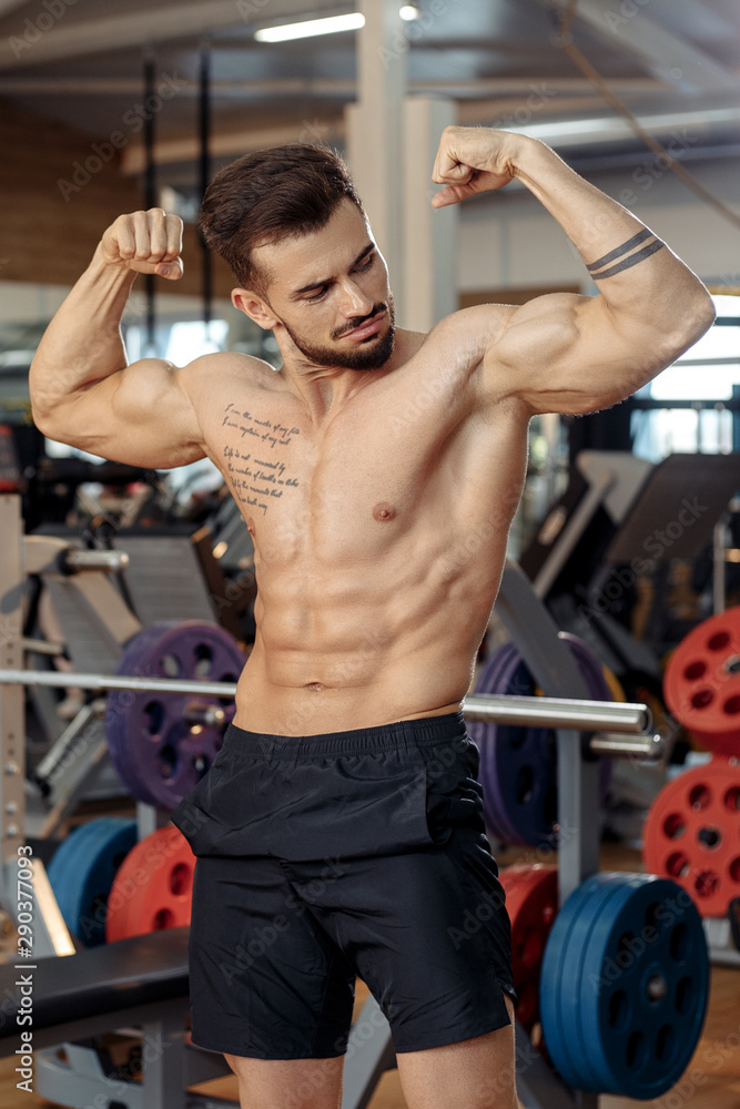 Muscular athletic young man bodybuilder fitness model show his biceps after exercises in gym. Muscular athletic young man bodybuilder fitness model show his biceps after exercises in gym.