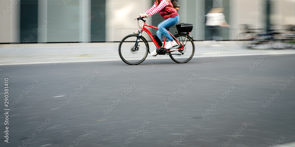 Obraz premium Frau fährt mit einem Pedelec im Straßenverkehr, Bewegungsunschärfe