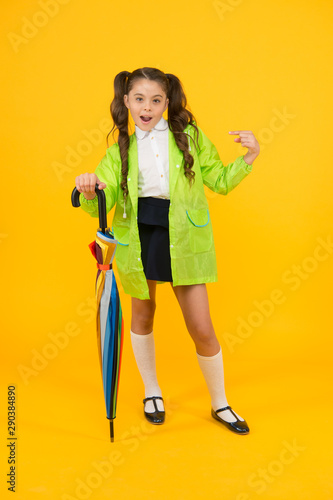 She a fashion victim. Cute schoolchild pointing finger with fashion look on yellow background. Little child in raincoat holding fashion umbrella. Rainwear and rainy day fashion