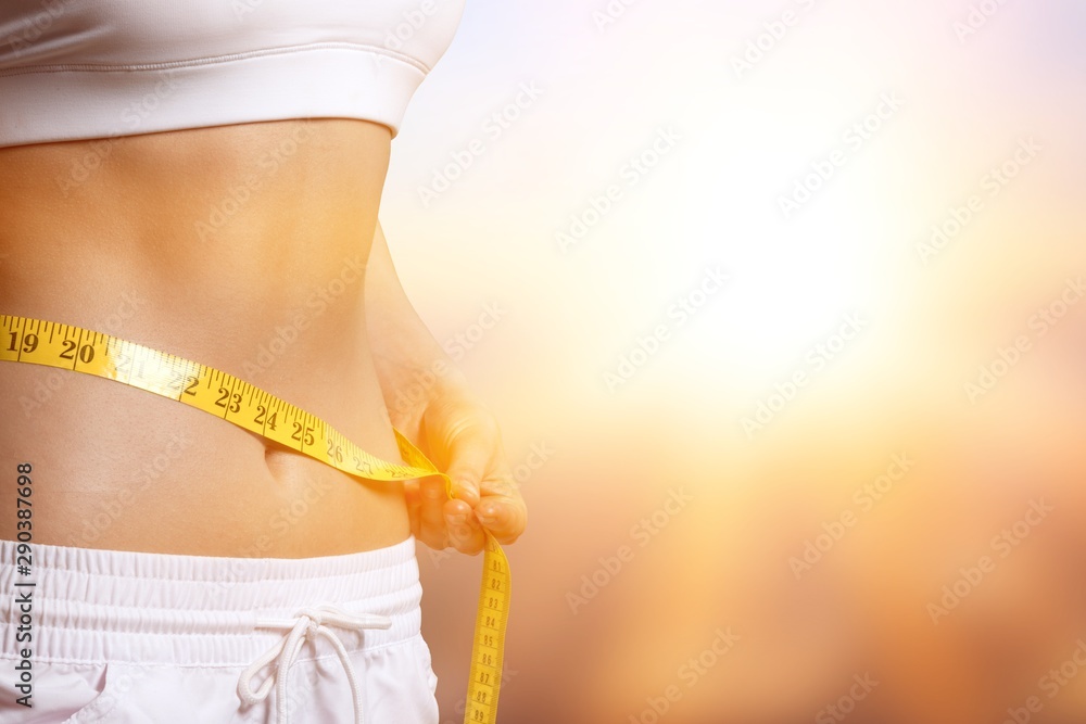 Slim young woman measuring her thin waist with a tape measure, close up - obrazy, fototapety, plakaty 