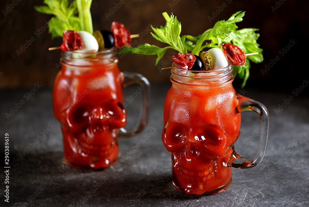 Bloody Mary cocktail in glass skull with celery sticks, pink salt, lime