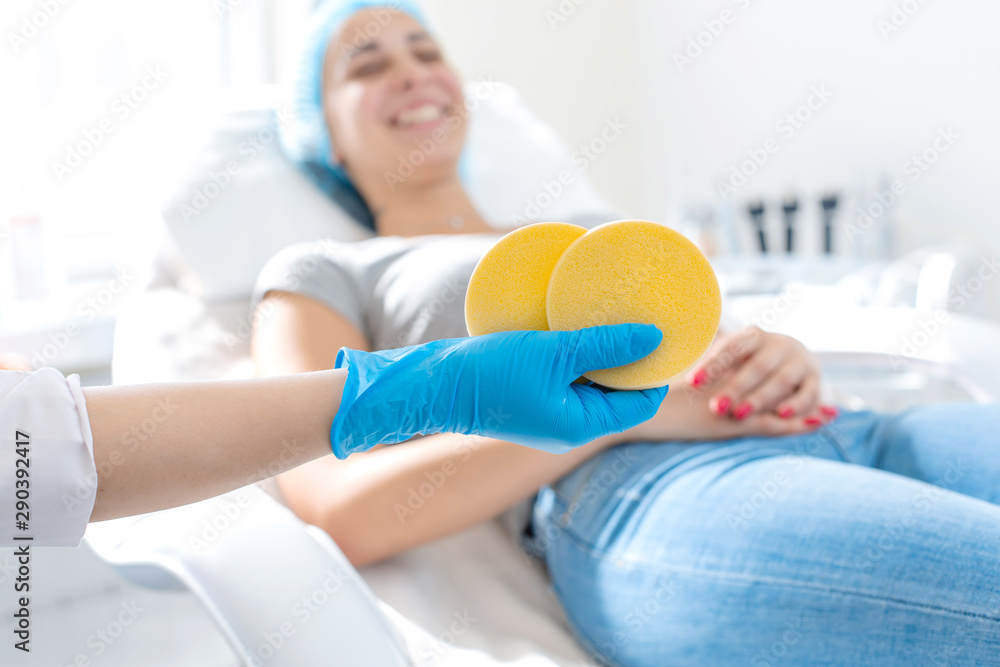 Obraz premium the hand of the beautician holds the massage pad against the background of a happy patient