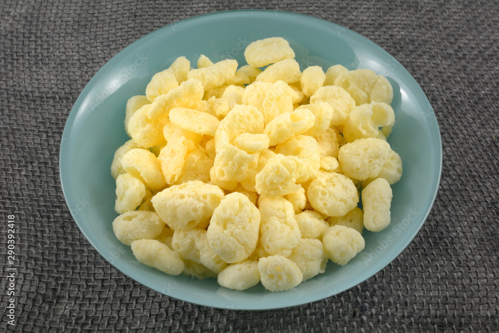 Dehydrated puffed gouda cheese pieces in blue snack bowl on rustic tablecloth Dehydrated puffed gouda cheese pieces in blue snack bowl on rustic tablecloth