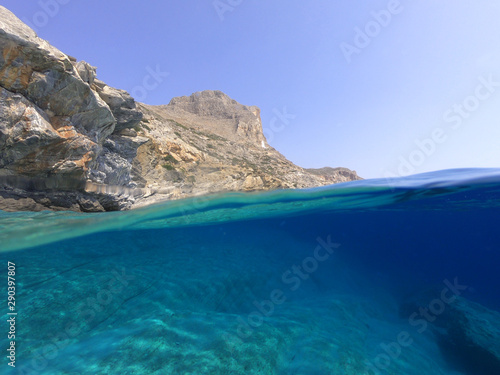 Above and below underwater photo of crystal clear sea paradise rocky seascape and small chapel of Agia Anna just next to iconic Hozoviotissa Monastery, Amorgos island, Cyclades, Greece © aerial-drone