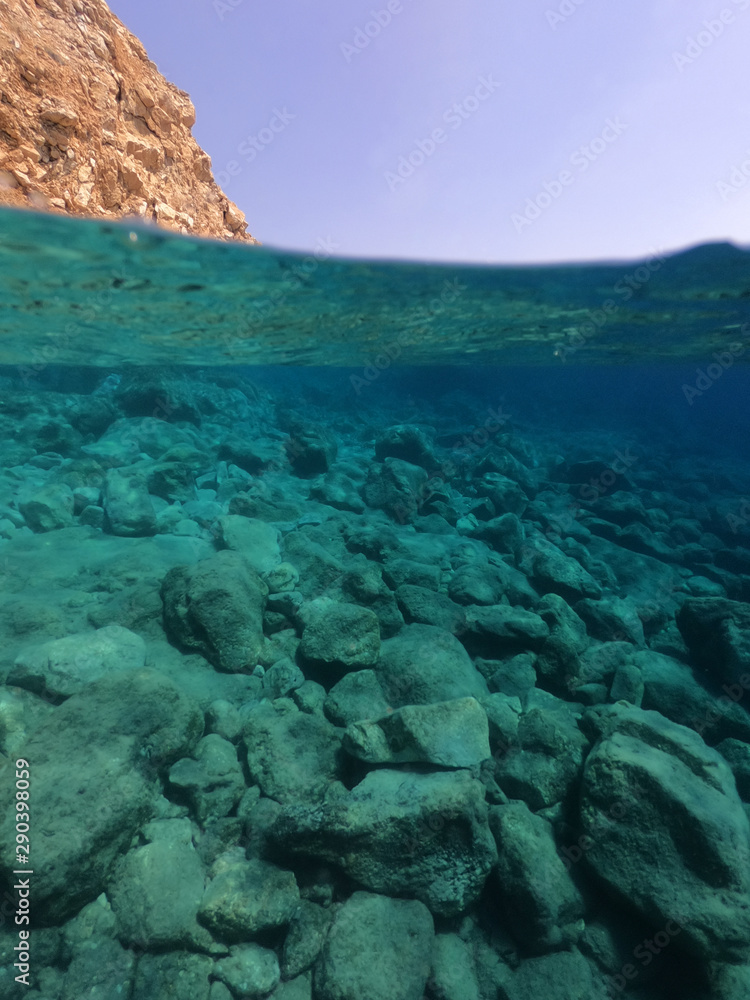 Beautiful underwater split above and below photo of rocky seascape with deep blue sky and clouds in tropical exotic island destination Beautiful underwater split above and below photo of rocky seascape with deep blue sky and clouds in tropical exotic island destination