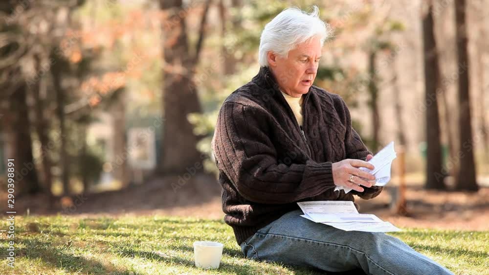 Senior Caucasian man sitting in grass and receiving good news in mail Senior Caucasian man sitting in grass and receiving good news in mail