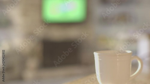 Steam rising from coffee cup with television in background