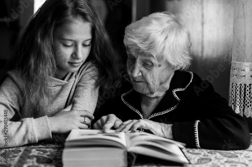Cute little girl with her grandmother reading a book together. Black and white photo.