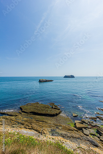 A panorama seascape view with rocky islands along the coast under a majestic blue sky and some white clouds