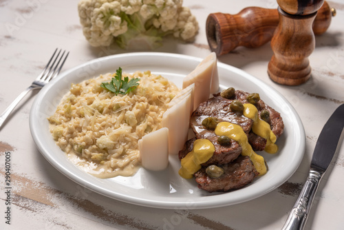 Risotto with filet mignon. Risoto and beef with capers and mustard in a white plate on wooden white background. Soft light. Italian food.