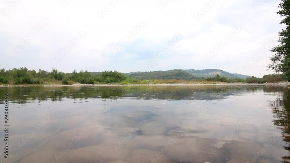 Water stream of a mountain river. It flows calmly in the valley. On the horizon are hills with forests. Water stream of a mountain river. It flows calmly in the valley. On the horizon are hills with forests.