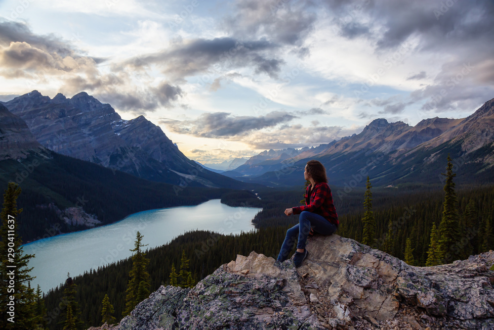 Adventurous girl on the edge of a cliff overlooking the beautiful Canadian Rockies and Peyto Lake during a vibrant summer sunset. Taken in Banff National Park, Alberta, Canada.