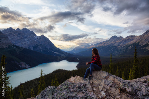 Adventurous girl on the edge of a cliff overlooking the beautiful Canadian Rockies and Peyto Lake during a vibrant summer sunset. Taken in Banff National Park, Alberta, Canada.