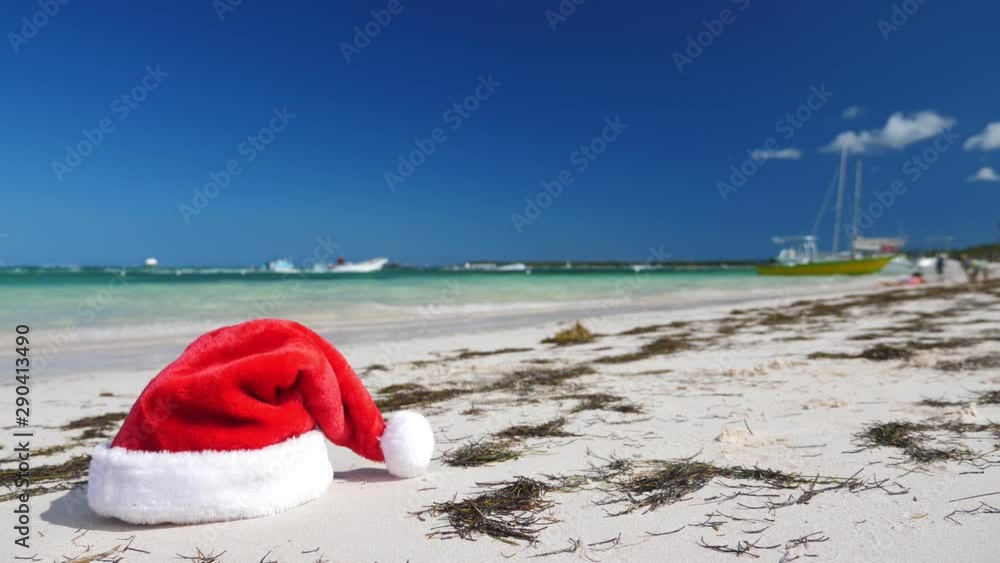 Christmas Santa Claus hat on tropical sandy beach with calm waves. Winter holidays. New Year celebration on caribbean island Christmas Santa Claus hat on tropical sandy beach with calm waves. Winter holidays. New Year celebration on caribbean island
