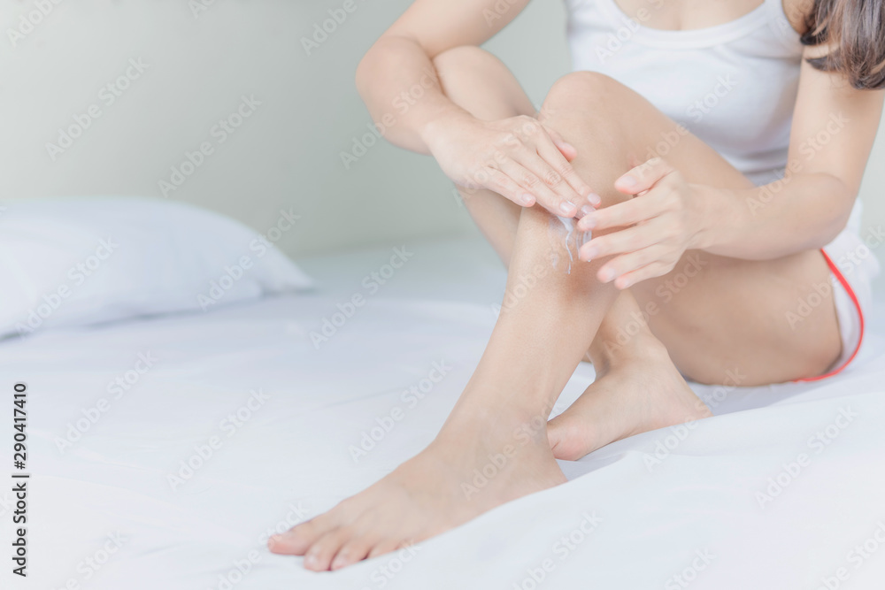 Beautiful young asian woman sitting on a bed stroking legs with soft smooth skin in the bedroom, girl applying touch body cream and lotion with treatment care concept. Beautiful young asian woman sitting on a bed stroking legs with soft smooth skin in the bedroom, girl applying touch body cream and lotion with treatment care concept.