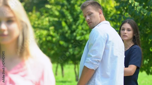 Young man looking at pretty woman during walk with girlfriend in park, jealousy photo