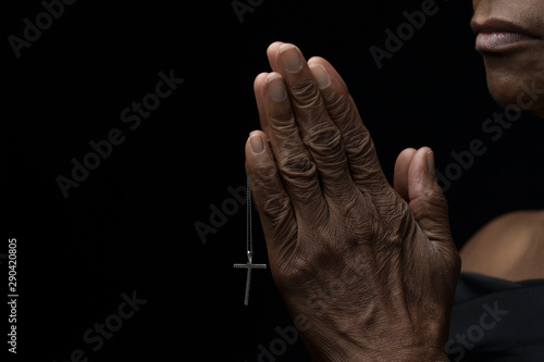 Religious and elderly african-american woman faithfully praying with hope while holding a cross