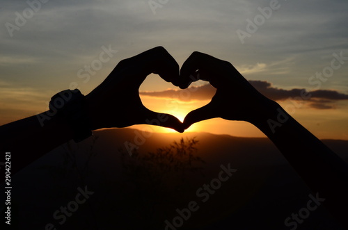 Two guys making hands in heart shape  And the background is in the evening the setting sun.
