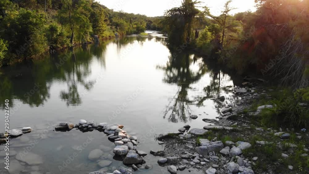 Flying low over a river swimming area at sunset; suns rays peering through trees. Rising above to reveal larger portion of river. - Aerial footage of the Blanco river in Wimberly, TX Flying low over a river swimming area at sunset; suns rays peering through trees. Rising above to reveal larger portion of river. - Aerial footage of the Blanco river in Wimberly, TX