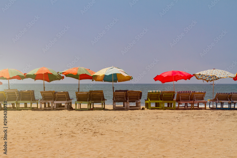 Row of covered wooden deck chairs with colorful umbrellas on the beach, toned with sunlight. Bright summer background. Holiday template.
