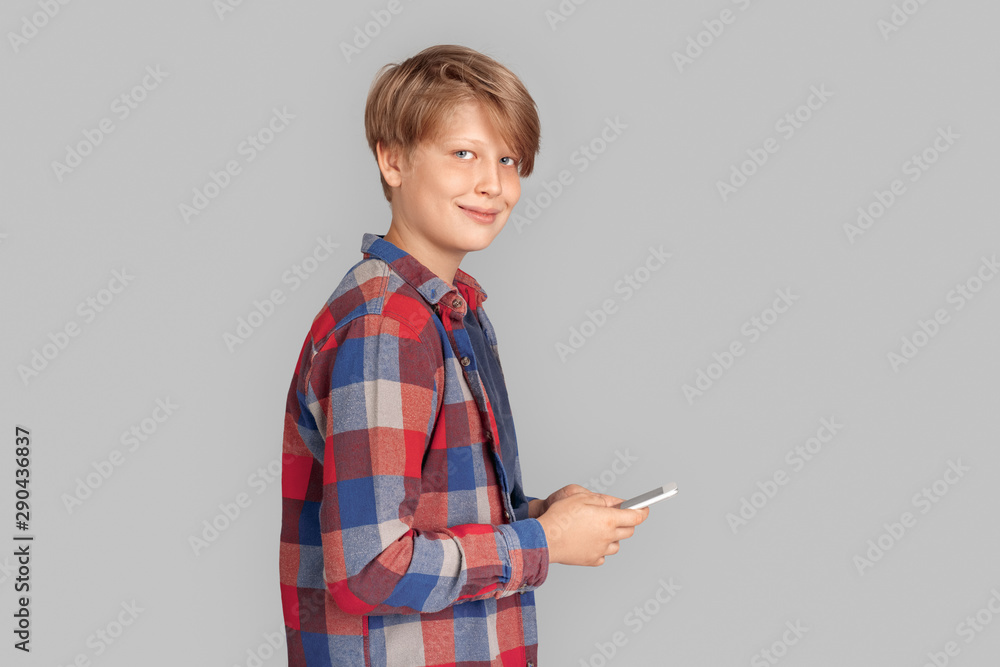 Freestyle. Young boy standing isolated on grey browsing phone smiling joyful Freestyle. Young boy standing isolated on grey browsing phone smiling joyful