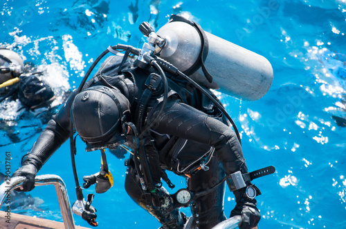 An unrecognizable woman in a wetsuit with a scuba gear rises to the deck of a yacht from blue sea water after diving. photo