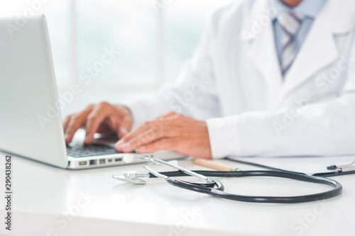 Senior doctor at his office in hospital working close-up blurred using laptop typing