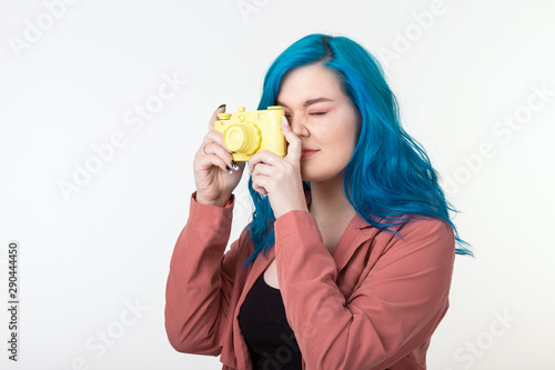 People, hobby and interests concept - Beautiful girl with blue hair hold yellow retro camera on white background