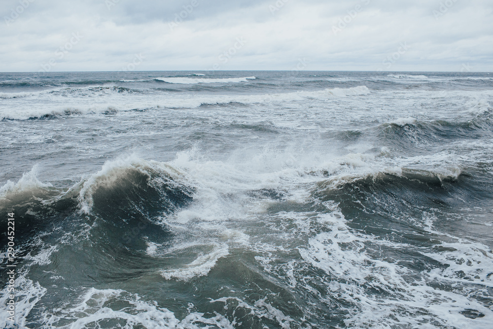 Fototapeta premium Waves Breaking and Spraying at High Seas and Strong Winds. Storm at the sea in autumn cloudy rainy day.