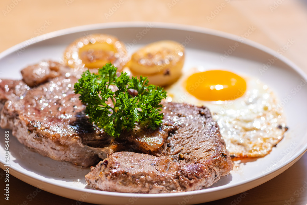 Close up and selective focus of meat beef steak Fried egg and onion in white plate on wooden table.