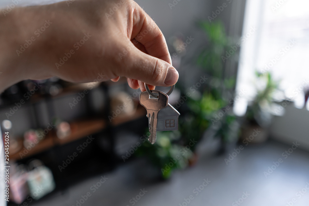 Fototapeta premium Concept of renting an apartment. House key in man hands. Young woman. Modern light lobby interior. Real estate, hypothec, moving home or renting property.