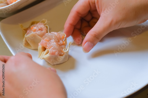 Close up and selective focus of hands cooking homemade making of Traditional chinese food dumpling called Shumai in Thailand called kanom jeep. Cooking by steam in bamboo basket.