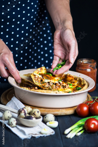 chef's hand cook tasty meat pie with carrots, onions and cheese in a baking dish on a dark background