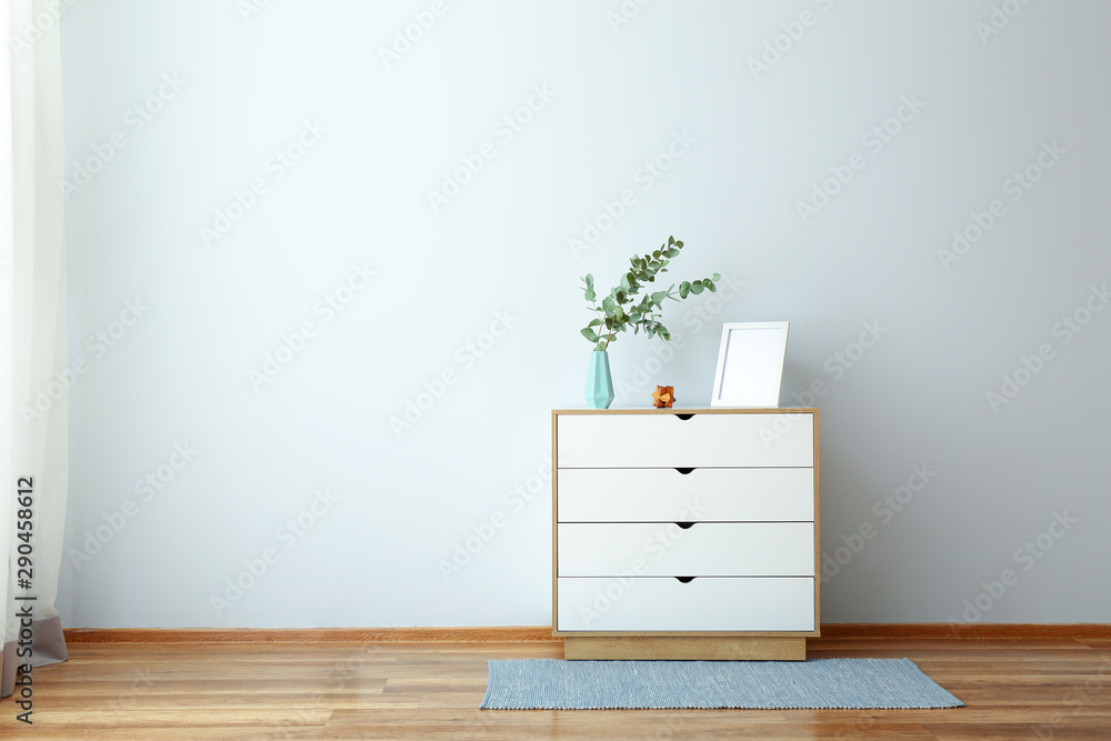 Chest of drawers with eucalyptus branches in vase near light wall - obrazy, fototapety, plakaty 