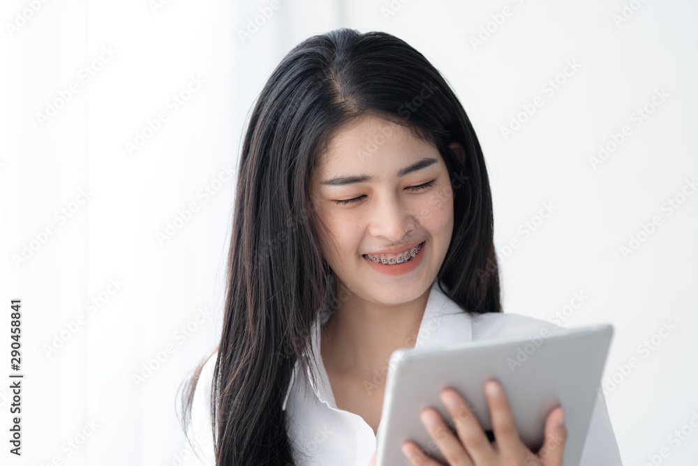 Beautiful Asian woman in white shirt using tablet near window in the morning. Beautiful Asian woman in white shirt using tablet near window in the morning.