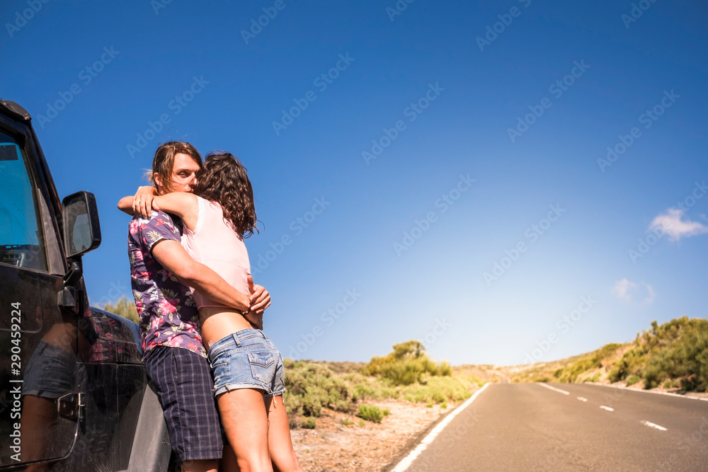 Coloured style caucasian young beautiful couple standing and hugging outside a black car during alternative travel vacation. together - concept of youthful and wanderlust for alternatie people