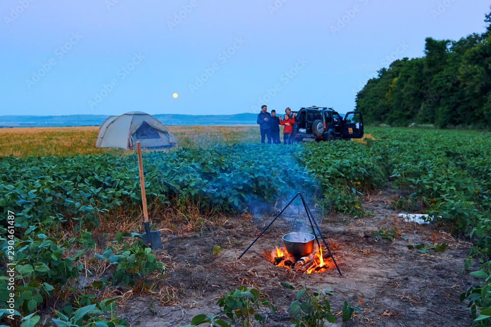Family traveling and camping, twilight, cooking on the fire. Beautiful nature - field, forest and moon.