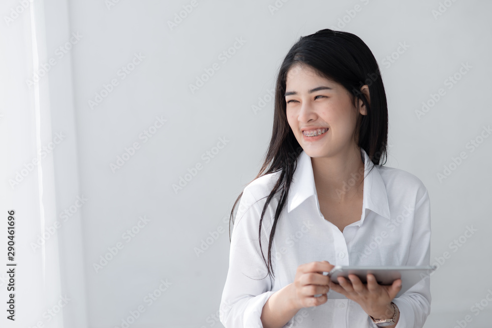 Beautiful Asian woman in white shirt using tablet near window in the morning. Beautiful Asian woman in white shirt using tablet near window in the morning.