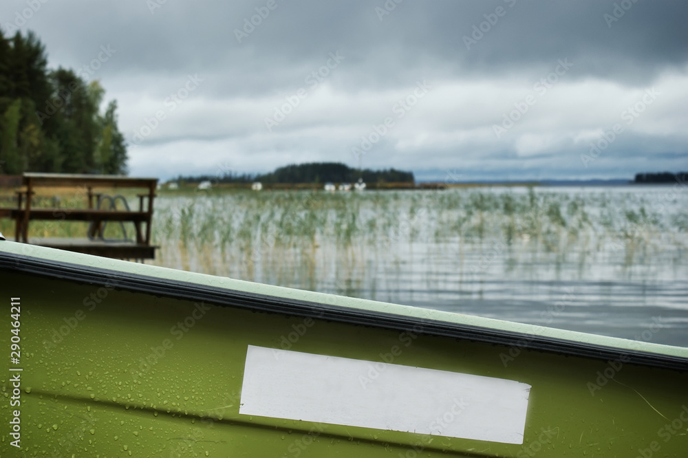 A board of the green rowing boat. In the background is a lake, pier and sky. Outside is cloudy autumn weather. Scandinavian lifestyle. There is a place for your logo.