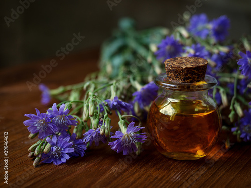 Small bottle of natural essential oil among blue flowers on wooden background. Organic cosmetic products, low key, selective focus