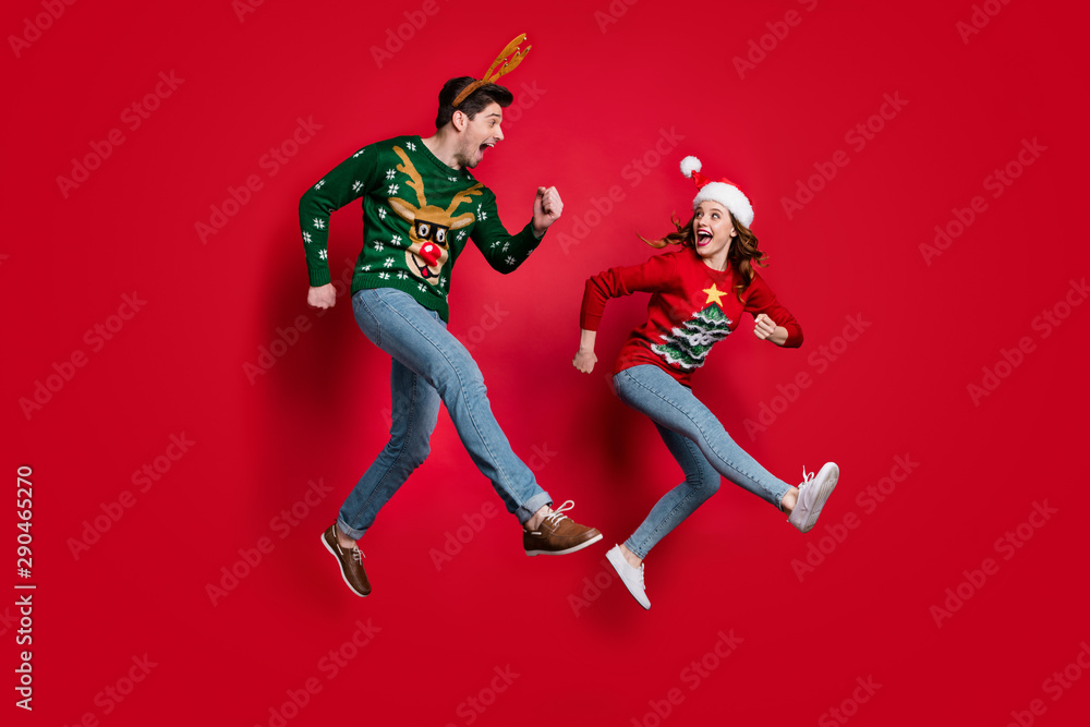 Full body photo of excited jumping couple rushing for x-mas discounts wear ugly ornament jumpers isolated red color background