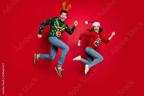 Full length photo of jumping couple excited by x-mas prices hurry buy costumes wear ugly ornament jumpers isolated red color background
