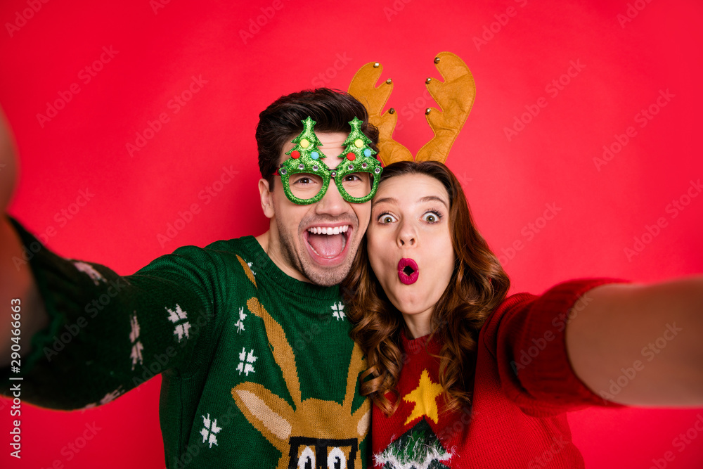 Obraz premium Photo of excited lady and guy chilling at x-mas costume party making selfies wear funky pullovers with ugly ornaments isolated red color background