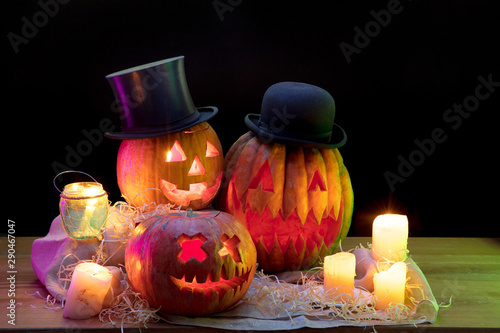 Halloween pumpkin head jack-o-lantern in hats with scary evil faces and candles. Seasonal illuminated decoration. Looks scary, colorful neon light and dark background. Holidays. Black friday, sales.