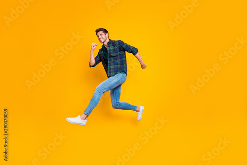 Full length body size side profile photo of cheerful positive funny trendy guy wearing jeans denim hurrying jumping up to sales isolated over vivid color yellow background
